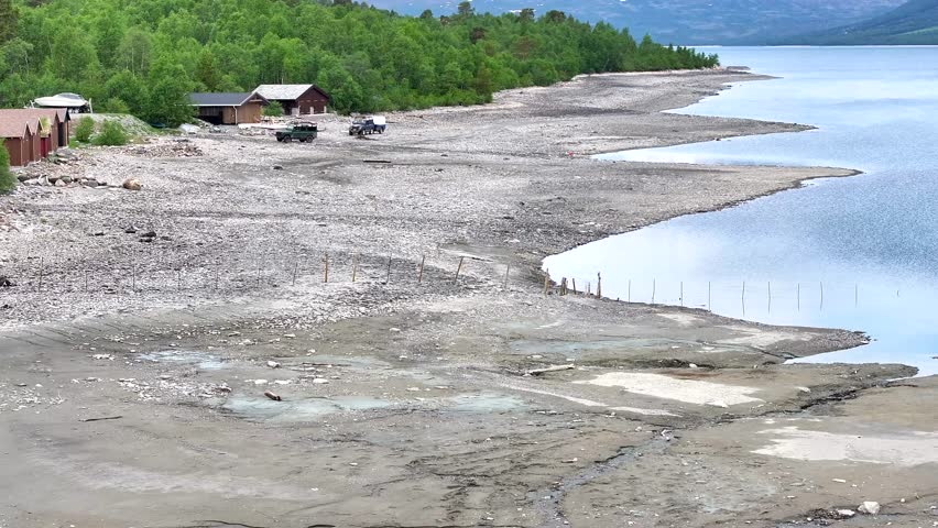Off-road cars drive along Gjevilvatnet near Osen in Oppdal. The lake is the main reservoir for Driva power plant. Beautiful Norwegian cultural landscape surrounded by high snow-capped mountains