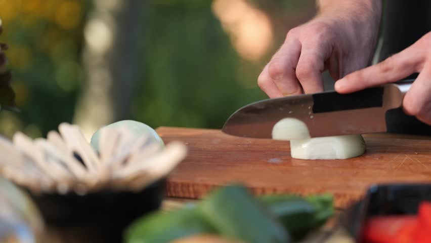 Young man chops onions on a wooden board in his garden close up