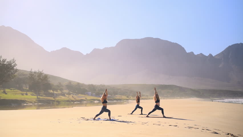 Beach, women and friends with meditation, yoga and wellness with sunshine, fitness and exercise with balance. Group, ocean and people with peace, healthy and workout with zen, chakra and mountains