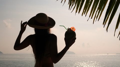 Silhouette of Young Tourist Girl Drinking Fresh Thai Coconut Cocktail at Tropical Beach. 4K, Slowmotion. Phuket, Thailand.