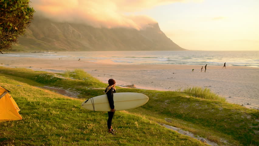 Sunset, freedom and woman with surfboard on beach with mountain, cloudy sky and view of ocean on holiday. Adventure, travel and girl on tropical vacation for surfing, peace and calm sea on island.
