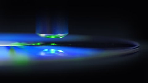 The green laser beam slides over the surface of the compact disk and reads the data on black background. The laser quickly finds the right sectors and take off information. Colorful reflections on the