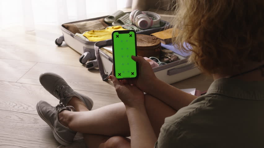 Smartphone with green chroma key mockup in hand of woman. Green screen phone, organized luggage for weekend trip. Flips deals on hotels and flights in mobile app, video for advertisement. Planning Royalty-Free Stock Footage #3391060873