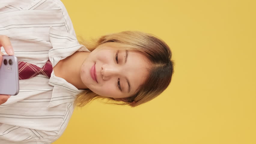 Vertical video, Laughing young woman dressed in shirt and tie looking at mobile phone isolated on yellow background in studio | Shutterstock HD Video #3391137253