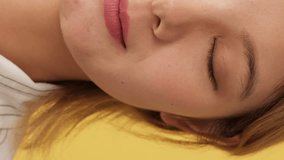 Vertical video, Close-up, half face of young woman opening eyes and looking at camera isolated on yellow background in studio