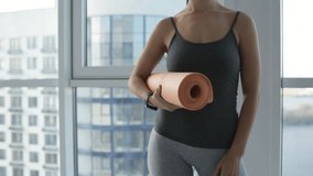 Relaxation. Close up of young woman standing in front of you while holding yoga mat in hands and preparing for meditation