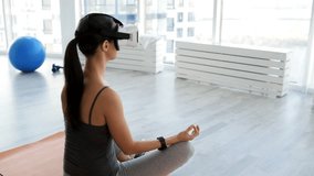 Power of imagination. Rear view of young woman sitting in yoga position and being concentrated while wearing virtual reality glasses