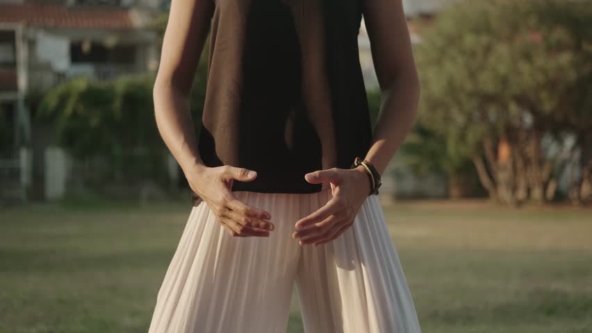 White woman in a black sleeveless tank top practices body position control with her eyes closed in the city park. System of breathing and movement exercises . Qigong. TaiJi. Static training.