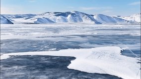 Video of winter landscape of frozen Baikal Lake in February cold sunny day. Сoastal mountains are covered with snow. Snow crust  on the surface of ice. Natural background. Winter travel and outdoors