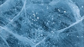 Video of winter natural ice texture of frozen Baikal Lake in cold February day. Blue ice surface with pattern of white cracks and bubbles. Natural background, top view, flat lay, blank, close-up