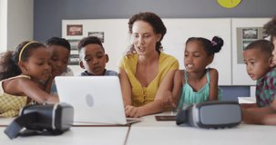 Video of happy caucasian female teacher and african american pupils using laptop and vr headsets. primary school education and teaching profession.