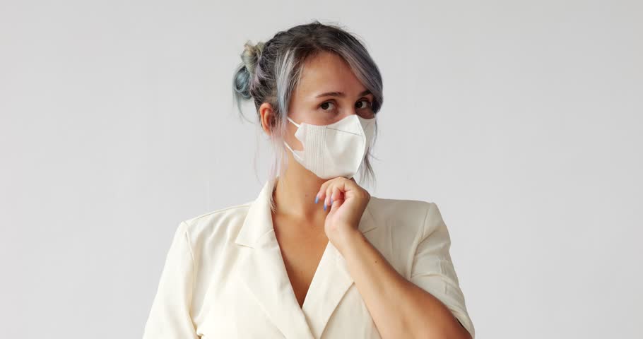 Woman tries on how she looks with white mask on her face, then decides to take it off and smiles right into camera, we see dental braces on her teeth. Portrait shot against a white background