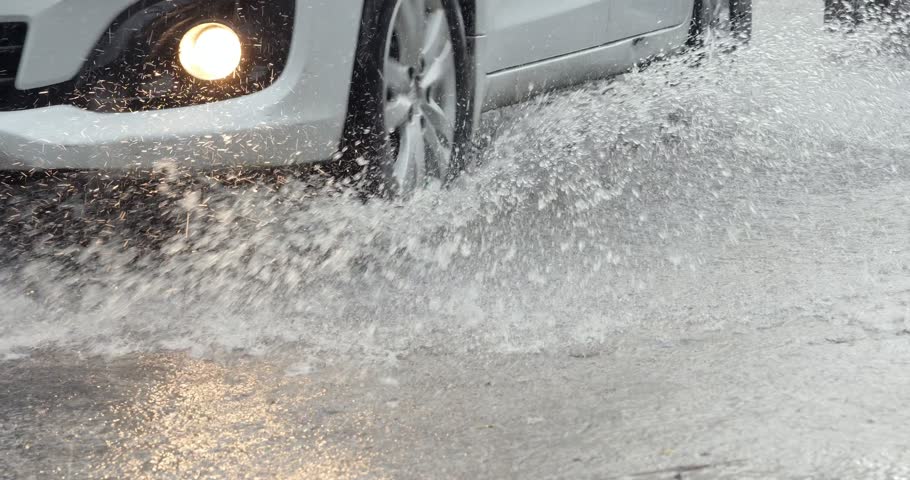 Heavy rain in Bali in rainy season, car is driving on a very wet road, the splash of water from under wheels, slow motion. A stream of water pouring right down the roadway of a narrow village street.