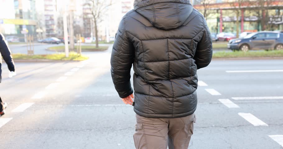Man in black jacket crosses road at pedestrian crossing. Pedestrian safety on road concept