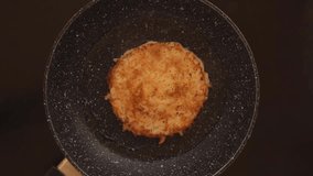 Top view wooden spatula turns a ruddy fried appetizing potato pancake in a frying pan. High quality FullHD footage. High quality FullHD footage