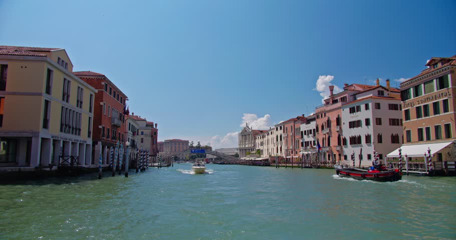 Bustling Grand Canal in Venice with boats navigating between ornate historic buildings and the iconic Ponte degli Scalzi in the background on a sunny day.