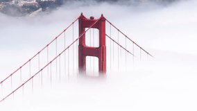 Cinematic bridge covered by dense thick fog with San Francisco downtown on background. Aerial red tall tower of Golden Gate Bridge in scenic white cloud USA.Helicopter overhead red bridge on sunny day