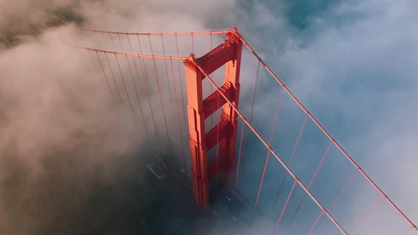 Epic motion background of magical fog cloud around red tower of Golden Gate bridge in San Francisco, USA 4K. Breathtaking aerial of Golden Gate Bridge lighten in golden sunshine at sunset or sunrise. Royalty-Free Stock Footage #3391351209