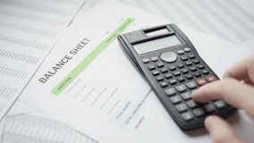Closeup of a balance sheet document with a calculator in use. The hands input financial data, emphasizing the meticulous process of financial calculations and record-keeping. - Powered by Shutterstock - Get 15% off with code: PIKWIZARD15