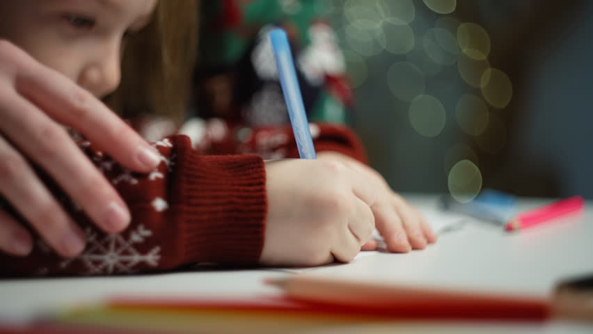A close-up of a child's hand writing with a pen on a piece of Santa's letter. Celebrating Christmas, gifts for the holiday, fairy tale atmosphere. High quality 4k footage