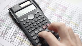 The video captures hands using a calculator over finance documents with numbers, illustrating the meticulous process of numerical calculations and financial analysis.