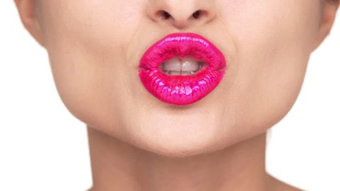 Face details of female lips covered by pink shining lipstick doing kissing gestures with smile over white background extreme closeup. Facial expressions