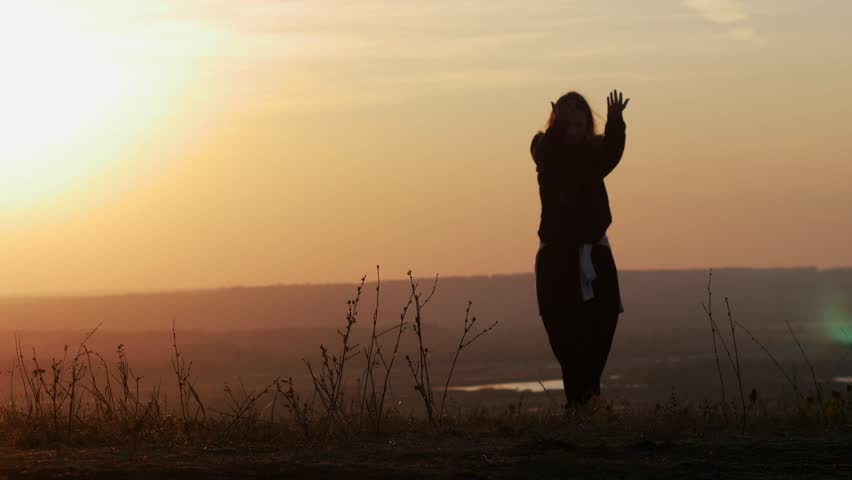 A girl dancing on a hill, against the background of the sun. Moving shot