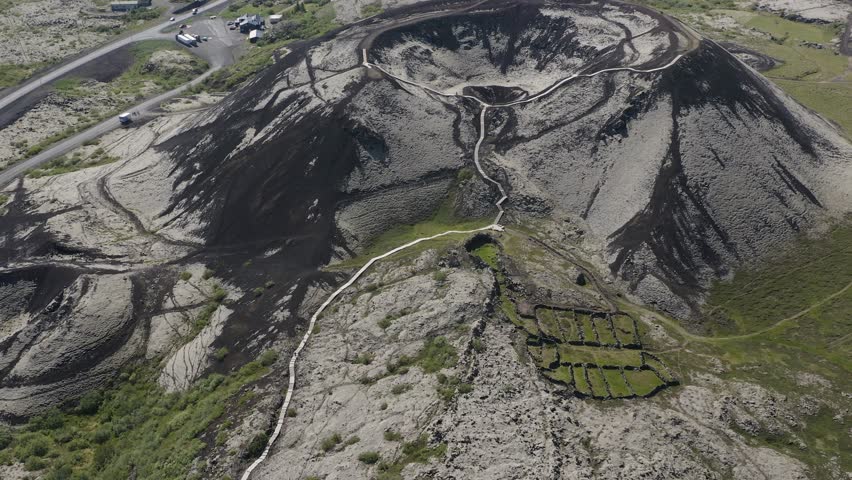 Drone video tilting up revealing the Grabrok crater with a small hiking path leading to the rim of this dormant volcano in Iceland