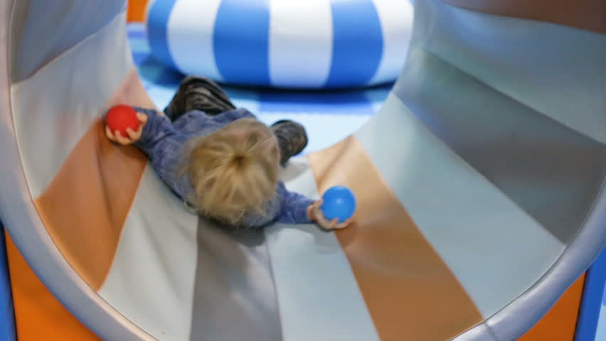 Little girl riding a ride, rotates the drum in the nursery. Satisfied, holding a ball. Close-up, real-time, artificial lighting, indoors, side view