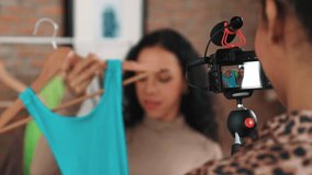 Two women influencer shoot live streaming vlog video review clothes crucial social media or blog. Happy young girl with apparel studio lighting for marketing recording session broadcasting online.