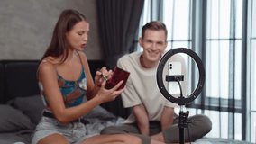 Young woman making beauty and cosmetic tutorial video content for social media using her boyfriend as model and light ring. Beauty blogger showing how to beauty care to audience or follower. Adit