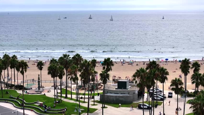 Flying over the palm tees to reveal Venice Beach in California, sail boats out in the ocean