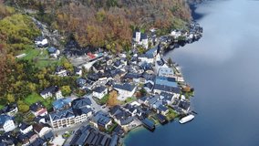 Smooth flight over the village of Hallstatt and Hallstatter See. Aerial view of lakeside houses, churches, boats and yellow and green trees on the mountainside. Wonderful autumn time. Austria in 4K