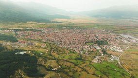 Aerial view of mountain resort town Bansko. Beautiful farming patchwork surrounds the town as well as mountain forests. Foggy weather adds haze in the distance.