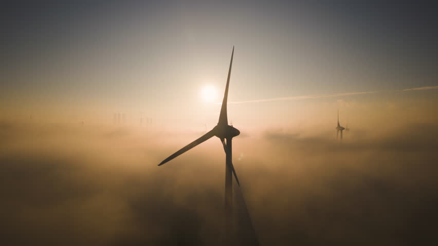 Silhouette of wind turbine casting shadows on clouds and fog below