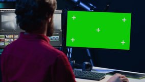 Video editor selects key frames to use in movie montage, using specialized software applications on green screen computer monitor. Freelancer using editing tools on chroma key PC, cutting footage
