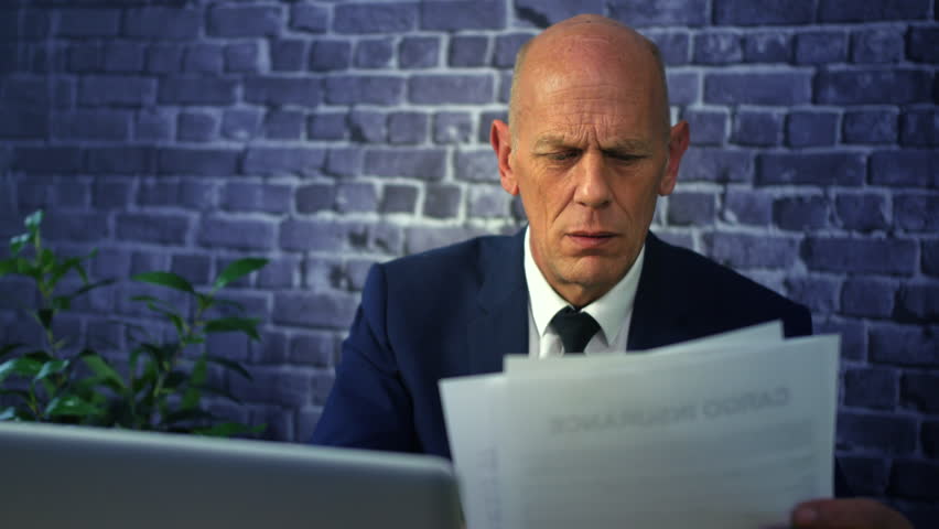 A stressed tired business man overworked with paperwork sitting at a desk with a laptop