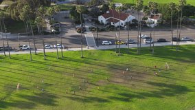 Drone shot of men playing football on green area with palm trees, Santa Barbara, California, USA. Overhead shot of male athletes training with soccer ball on sunny day. Sport concept, 4k footage 