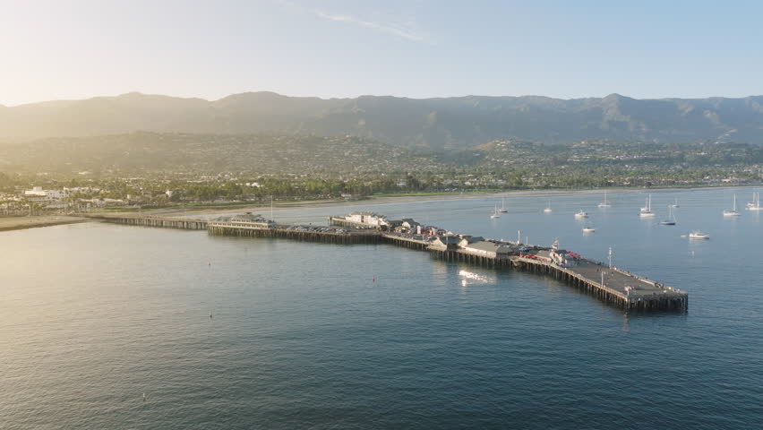 Birds eye view of picturesque landmark Stearns Wharf in sunset light of Santa Barbara harbor, California, USA. Amazing shot of city located along the Pacific Ocean coast and mountains, 4k footage  Royalty-Free Stock Footage #3391607983