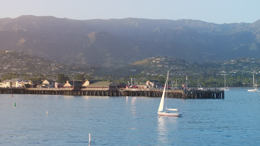 Scenic view of sailboats floating near Stearns Wharf, Santa Barbara, California, USA. Old wooden pier in city harbor. Picturesque shot of mountain hills with city buildings at the sunset, 4k footage  Royalty-Free Stock Footage #3391609141