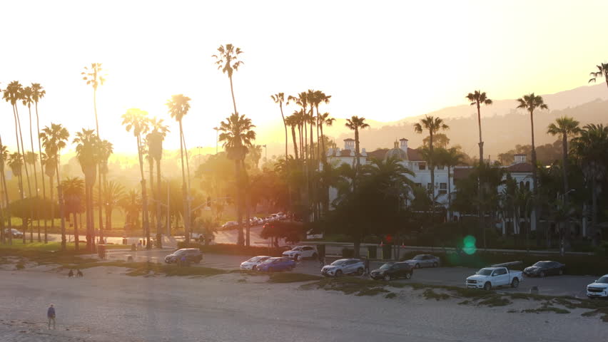 Aerial view of cars parked at the beach of Santa Barbara, California, USA. Overhead shot of tourists walking on beach. City buildings surrounded mountains and Pacific Ocean at sunset, 4k footage  Royalty-Free Stock Footage #3391609929