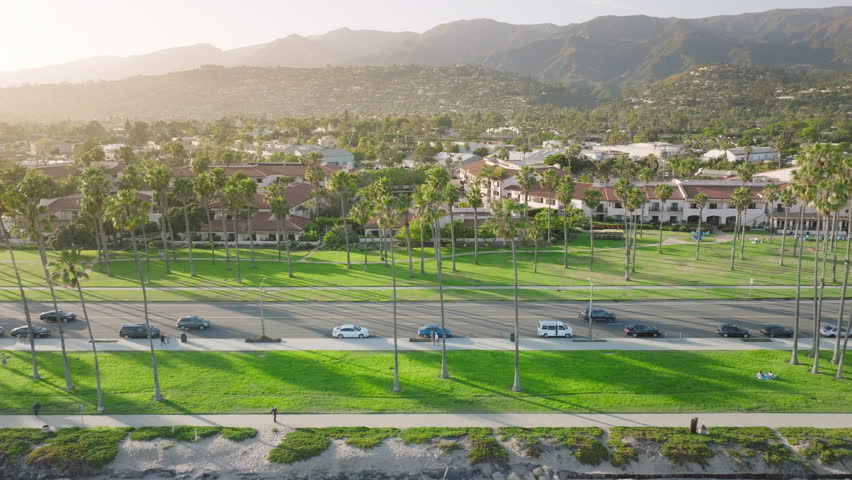 Drone shot of city life of Santa Barbara at the sunset, California, USA. Overhead of cars driving on street with palm trees. Residential houses and buildings with mountains on background, 4k footage  Royalty-Free Stock Footage #3391611619