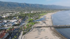 Birds eye view of Santa Barbara shoreline with city skyline, California, USA. Drone flying along resort city surrounded green mountains. Aerial shot of sandy beach located at Pacific Ocean, 4k footage
