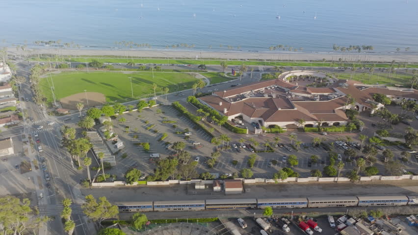 Aerial view of passenger train driving in the city of Santa Barbara, California, USA. Overhead shot of city transport and residential buildings. Pacific Ocean looking in the distance, 4k footage  Royalty-Free Stock Footage #3391618691