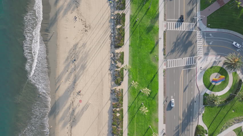 Top view of Santa Barbara beach and traffic, California, USA. Drone shot of Pacific Ocean waves rolling on coast. Cars driving on city road at seaside. Palm trees growing along the beach, 4k footage  Royalty-Free Stock Footage #3391619693