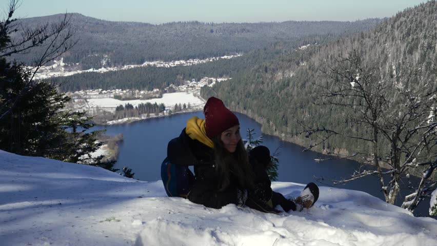 A young woman lays on the snow to relax after reaching the viewpoint over Lake Longemer in the Vosges Mountains. 