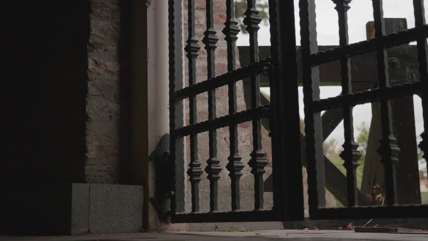 man with leather shoes and jeans enters a dark room after he walks through the wrought iron gate 96