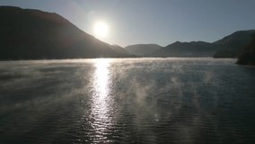 Flying fast and low over misty lake surface towards silhouetted mountains at sunrise in autumn. Ullswater, English Lake District, Cumbria, UK. - Powered by Shutterstock - Get 15% off with code: PIKWIZARD15
