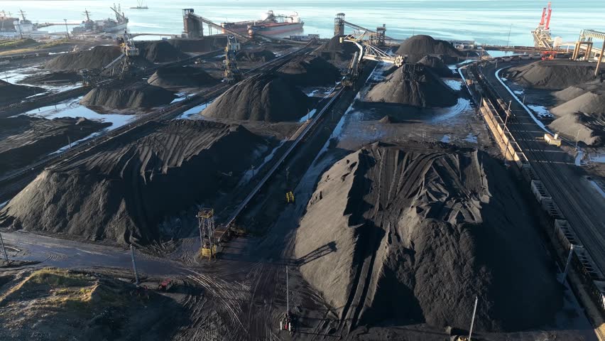 Coal port with loading cranes, conveyors, stockpiles, and a bulk carrier. Aerial view.