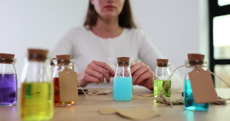 Female scientist hangs paper tags on small jars of colored liquids. Conducting experiment and extracting medicine from sample to cure serious disease in laboratory Royalty-Free Stock Footage #3391703613